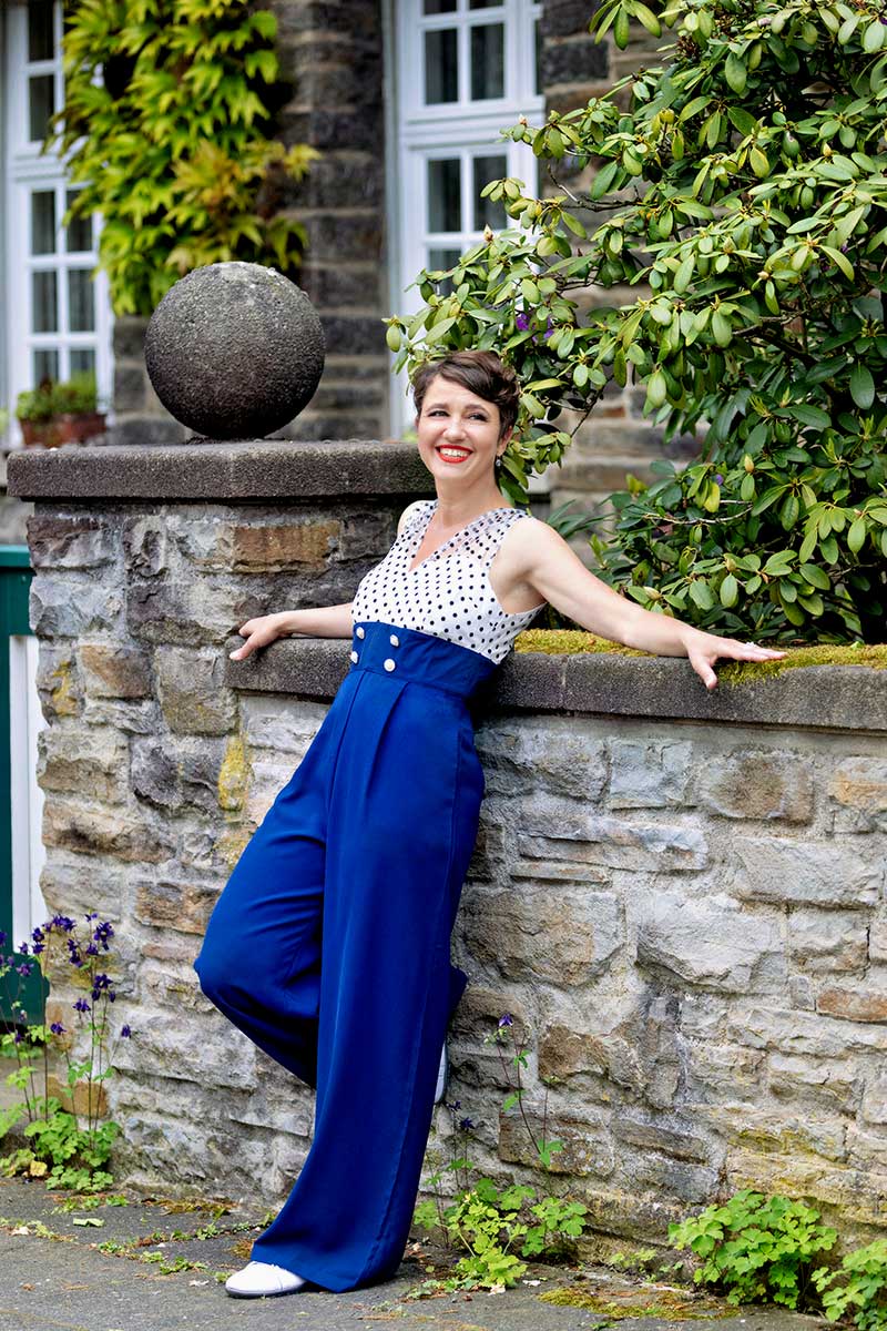 Sandra lehnt in Dortmund an einer alten Mauer in einem Vintage-Jumpsuit